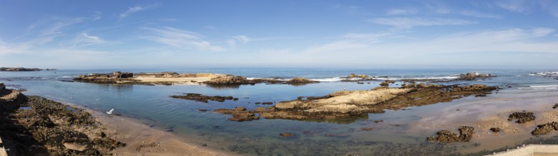Tranquil coastal scene with shallow water and rocks under clear sky