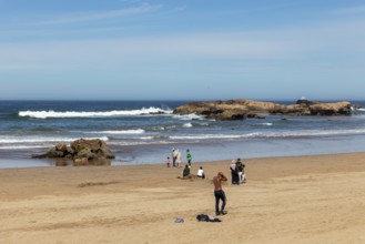 Quiet sandy beach with people and rocks in and around the clear blue sea