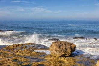 A quiet coastal scene with rocks and splashing waves under clear skies