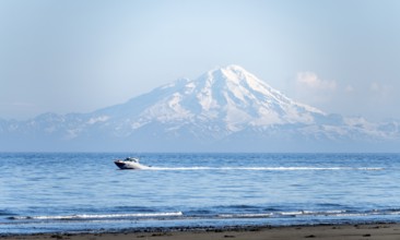 View over Cook Inlet to white mountain peaks of Mount Redoubt, motor boat rides on the ocean,