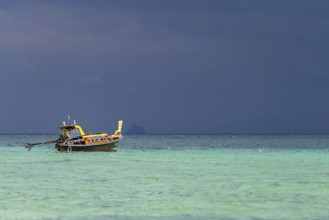 Longtail boat (Thai: Ruea Hang Yao) on the beach, behind it an approaching thunderstorm, Koh Ngai