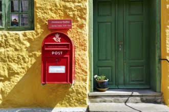 Post office, façade detail, red mailbox with post horn and crown, green wooden door, yellow wall,