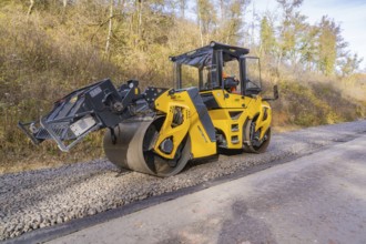 Yellow road roller on gravel road in autumn landscape during construction, track construction of