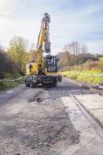 Yellow excavator lays tracks in autumn landscape, preparation of track work, track construction of