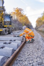 Workers lay concrete ties along a long railway line in an autumn landscape, track construction of