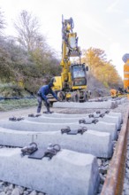 Workers use an excavator to lay concrete blocks along the tracks in autumn surroundings, track