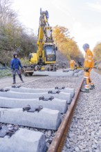 Construction workers lay concrete ties with a yellow excavator on a railway line in autumn, track