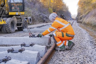 A construction worker wearing glowing safety clothing works on sleepers along the railway line,