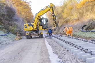 Workers and an excavator lay tracks in an autumn environment, track construction of the Hermann