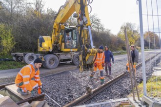 Construction workers in orange clothing work next to a yellow excavator on a railway line, track