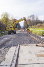 Construction workers lay tracks on a construction site while a yellow excavator assists. Autumn