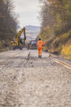 Road construction with construction workers and cranes on a gravel road in autumn, track