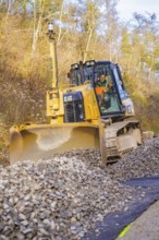 Bulldozer with a large shovel moves gravel on a construction site, track construction of the