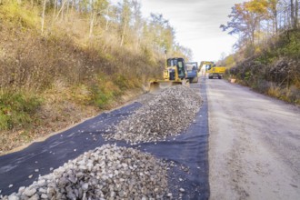 Several construction machines move gravel on a country road in autumn, track construction by the