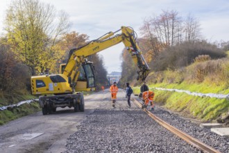 Yellow excavator on a construction site in autumn, workers laying tracks on gravel, Hermann Hesse