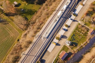 View from above of a train station with an adjacent street and autumnal greenery in the area, new