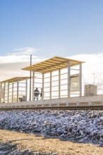 Two people at a modern bus stop under blue sky, new Hermann Hessebahn railway station, Ostelsheim,