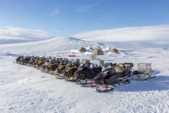 Snowmobiles, snow scooters at Arctic expedition camp with tents protected by tripwire fence against