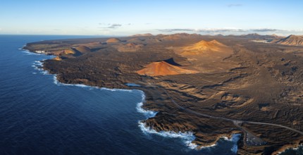 Coast with lava fields, volcanic landscape near Los Hervideros with red volcano Montaña Bermeja, in