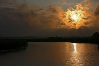 Dramatic sunset behind clouds over a quiet river with golden reflection, Peenetal nature park Park,