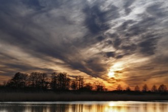 Dramatic sunset sky with trees and soft reflection in water, Peenetal nature park Park,