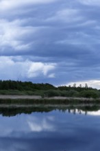 Cloudy sky over a quiet river with trees in the background, Peenetal nature park Park,