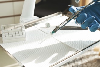 The dentist's hand, in a blue glove, holds a carpal syringe on a tray, ready for a medical