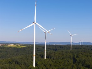 Wind turbines tower over a wooded landscape, dominated by clear skies, near Schorndorf, Remstal,