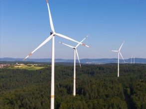 Three wind turbines rise above a green forest under a clear sky, near Schorndorf, Remstal,