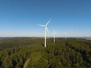 A series of wind turbines on a wooded hill under a wide blue sky, near Schorndorf, Remstal,