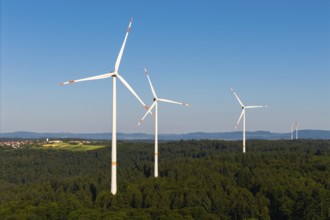 Wind turbines stand in a wooded landscape under a wide blue sky, near Schorndorf, Remstal,