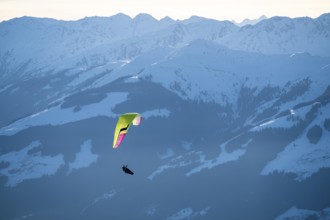 Paragliders flying over snowy mountain peaks in winter in evening light, Kitzbühel Alps, Tyrol,