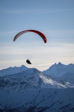 Paragliders flying over snowy mountain peaks in winter in evening light, Kitzbühel Alps, Tyrol,