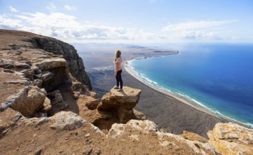 Young woman enjoying the view from the Risco de Famara cliffs to Famara beach, Playa de Famara with