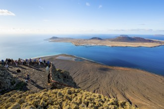 View of La Graciosa island with volcanic craters in the evening light, tourists on an observation