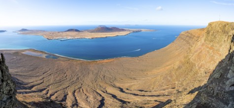View of steep cliffs by the sea and island of La Graciosa with volcanic craters in the evening