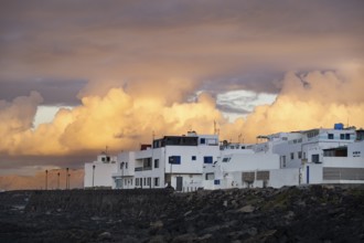 Black coast of volcanic rocks behind typical white houses of the village of La Santa, at sunset,