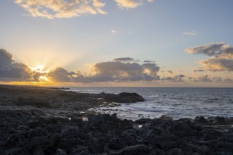 Dramatic cloudy sky with sunbeams at sunset, seaside coast with volcanic rocks, La Santa,
