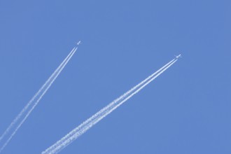 Two jet passenger aircraft flying in a blue sky with contrails or vapour trails behind, England,