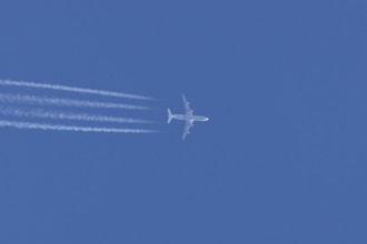 Jet commercial passenger aircraft flying in a blue sky with contrails or vapour trails behind,