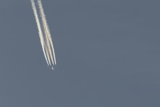 Jet passenger aircraft flying in a blue sky with contrails or vapour trails behind, England, United