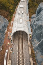 Close-up of tunnel construction site with workers and surrounding autumnal forests,