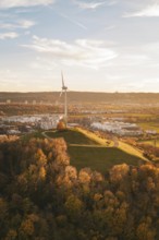 A wind turbine on a hill surrounded by autumn trees and urban landscape, Grüner Heiner, Korntal,