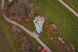 An observation tower in the middle of a rural landscape with fields and buildings, surrounded by
