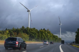 Tourist traffic on the A9 motorway during thunderstorms, wind turbines in the pine forest in the
