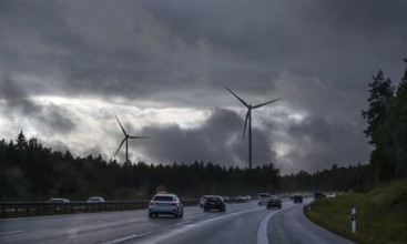 Tourist traffic on the A9 motorway during thunderstorms, wind turbines in the pine forest in the