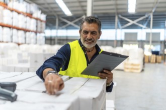 Logistics manager smiling while using a barcode scanner and clipboard checking shipment boxes in a