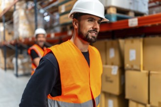 Man wearing an orange safety vest and white hard hat, working at a logistics warehouse with shelves
