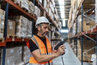 Warehouse worker wearing safety hardhat and vest scanning product packages on shelves in a large