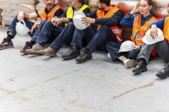 Group of diverse warehouse workers sitting on the floor taking a break, feeling exhausted after a